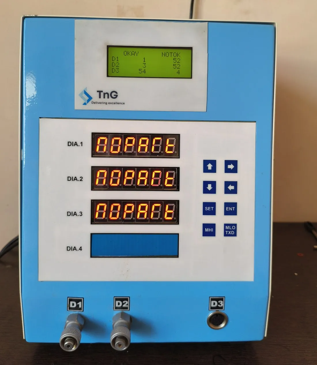 TnG digital gauge with three red 7-segment readouts labelled DIA 1 to DIA 3, a green LCD panel and keypad, on a blue enclosure.